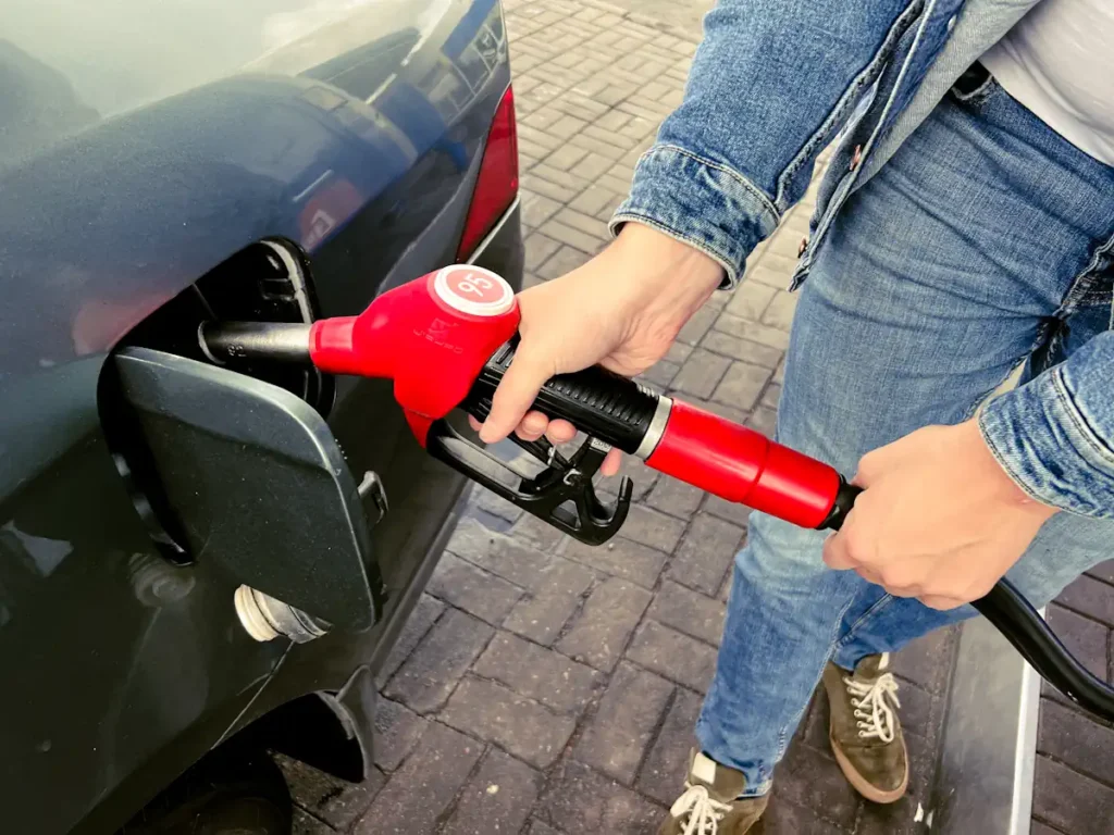 Une personne qui tient une pompe de carburant rouge pour ajouter du carburant dans sa voiture