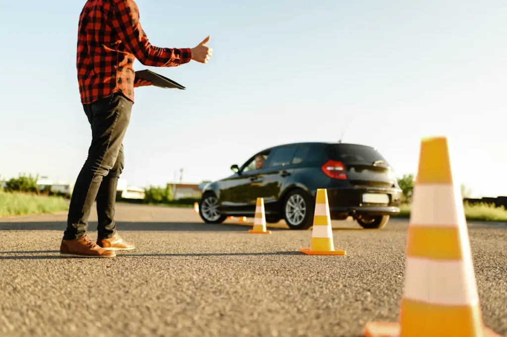 Une personne qui lève le pousse en tenant un carnet dans la main face à un conducteur qui roule sans toucher des cônes de signalisations
