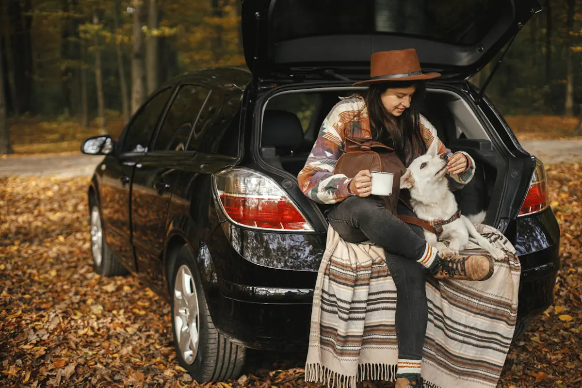 Une jeune femme installée dans le coffre ouvert d'une voiture noire avec son chien