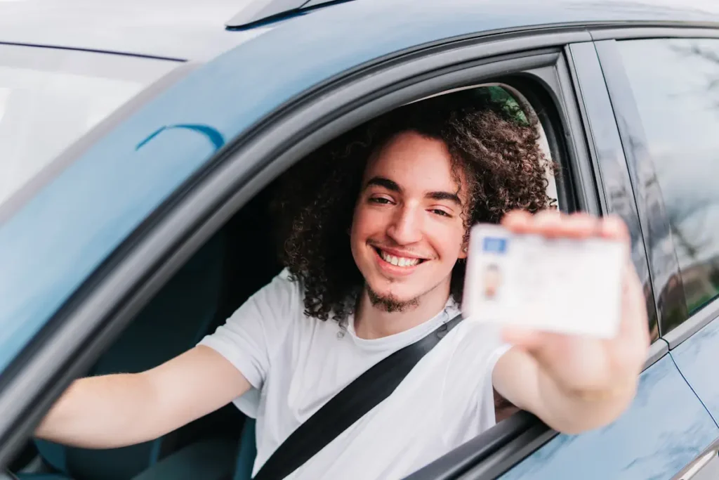 Un jeune derrière son volant qui montre un permis