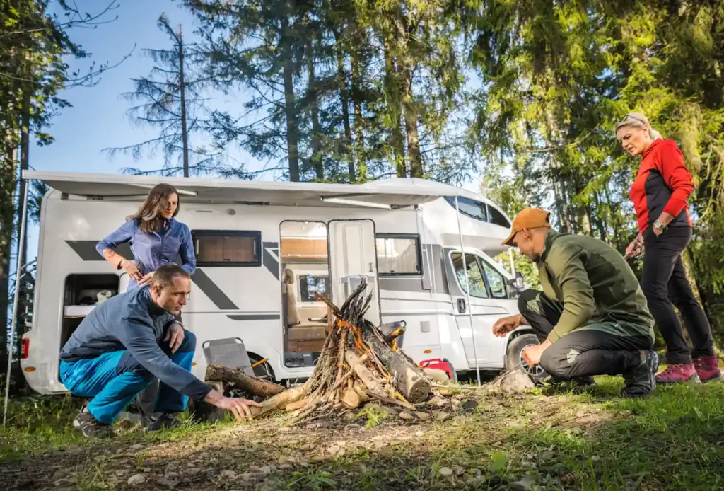Une femme et deux hommes qui allume un feu en pleine forêt à côté de leur camping-car