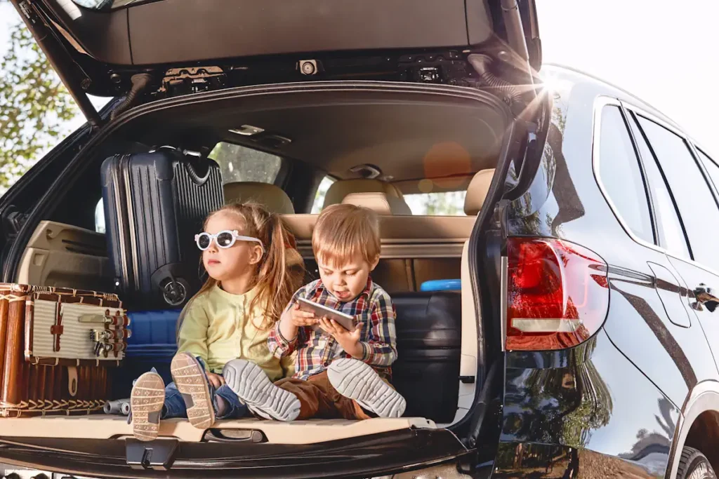 Des enfants installés dans le coffre d'une voiture ouverte ave des valises