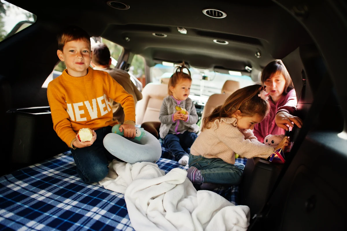 Des enfants installés à l'arrière d'une voiture avec le sol protéger par une couverture en carreau bleu et blanc