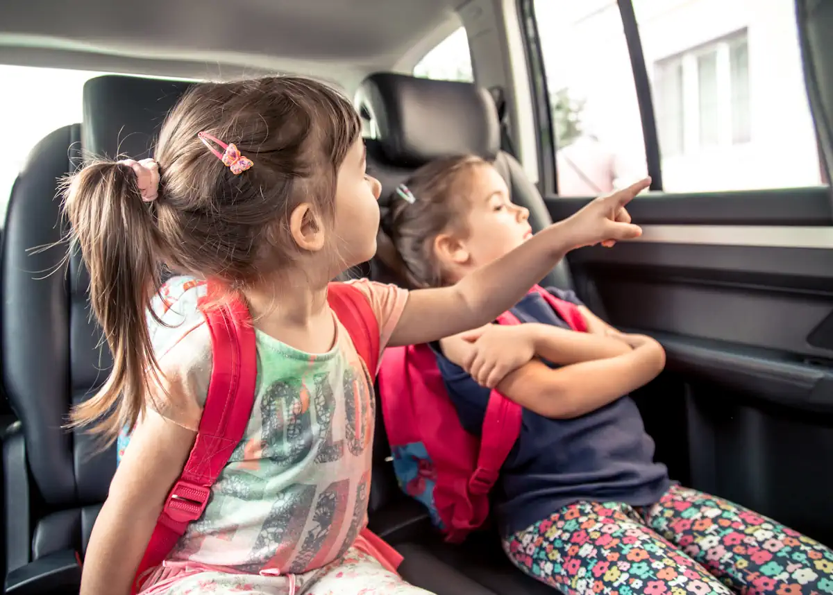 Une petite fille à l'arrière d'une voiture assise à côté d'une autre petite fille qui montre quelque chose par la fenêtre