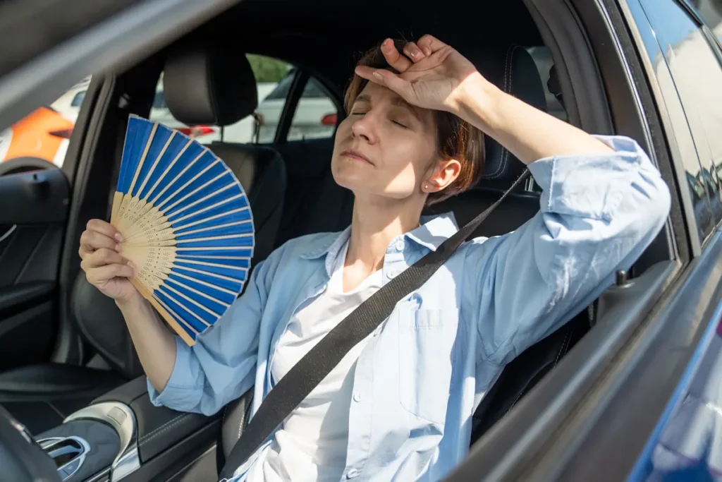 Une femme qui se rafraîchit avec un éventail dans sa voiture