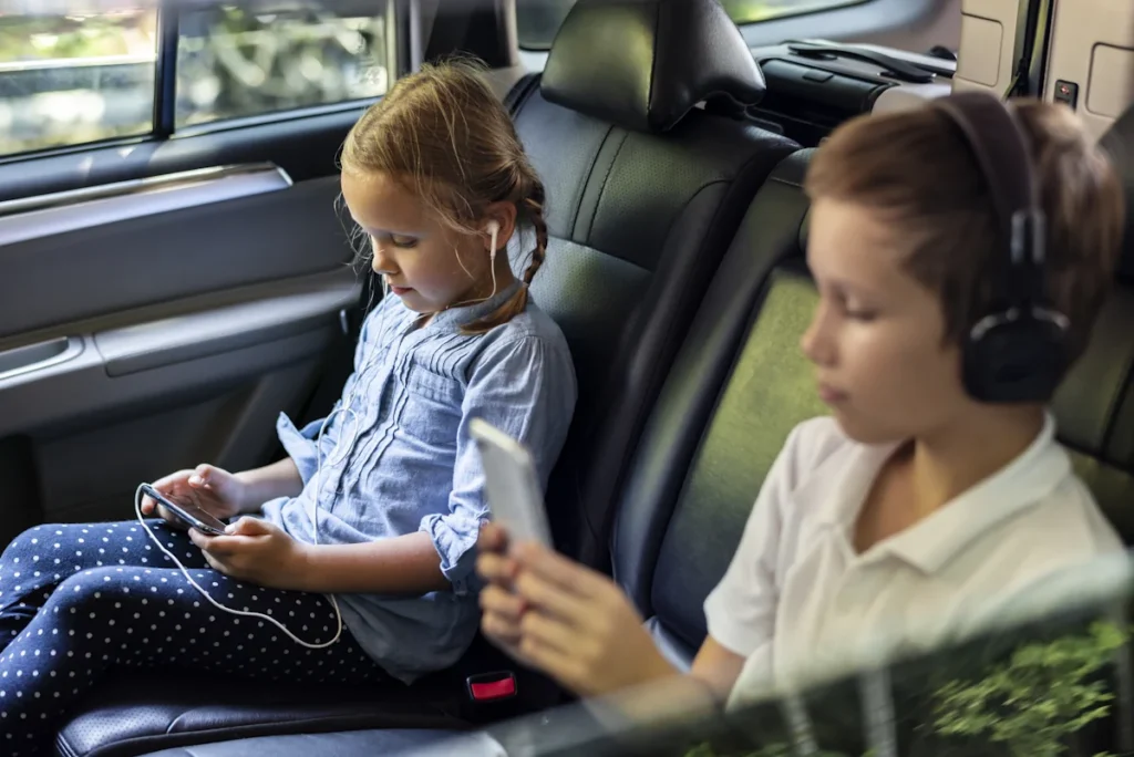 2 enfants installés à l'arrière d'une voiture qui regarde chacun les écrans
