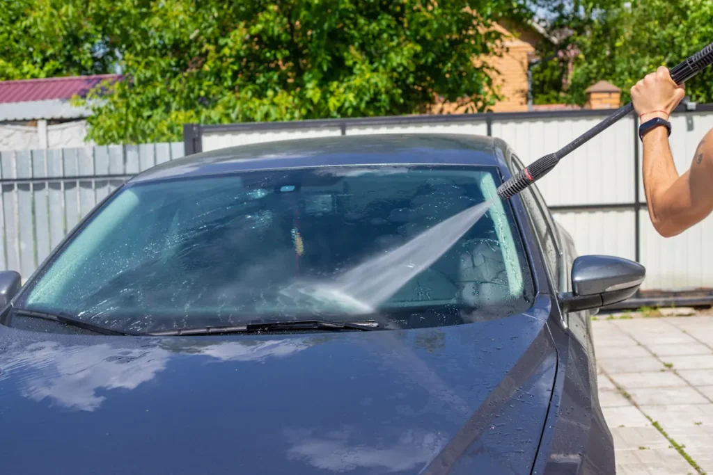 Une personne qui nettoie un parebrise avec un jet d'eau