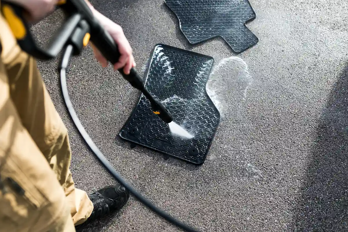 Un homme qui nettoie des tapis de sol de voiture avec un jet d'eau