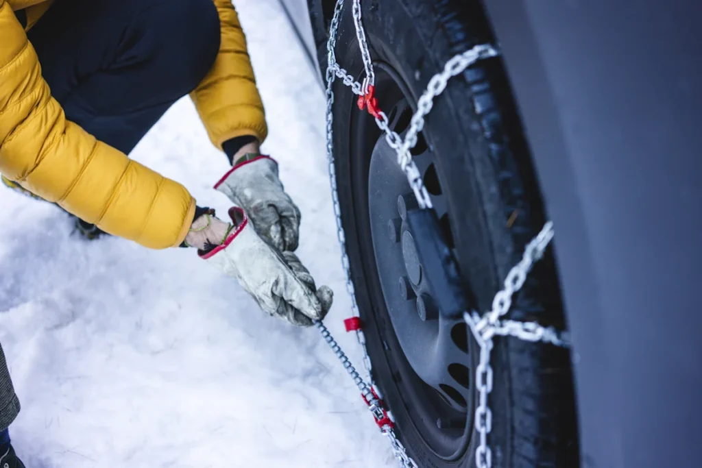 Un homme qui met en place une chaîne neige en composite sur ses pneus