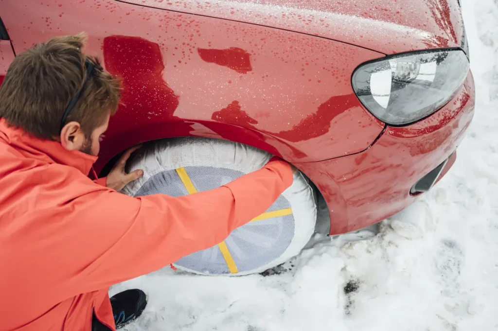 Un homme qui met une chaussette à neige sur les pneus de sa voiture